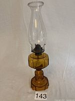 Full view of vintage oil lamp showing amber glass base and clear glass chimney against a plain background.