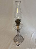 Single vintage glass oil lamp on neutral background showing entire lamp with base, oil reservoir, burner, and chimney.