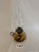 Full view of vintage glass oil lamp with clear chimney, amber glass base and brass burner.