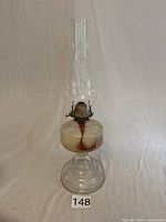 Full view of vintage oil lamp showing clear glass base, fuel reservoir, metal burner, and tall glass chimney.