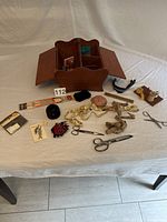 Wooden sewing box with hinged side panels open and various sewing accessories displayed around it on a white cloth surface.