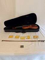 Violin, case, bow, strings, and rosin laid out on a white surface.