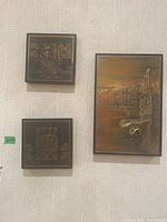 Photo showing two square indigenous style metal relief artworks and one larger rectangular painting on a patterned wall.