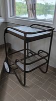View of metal patio bar cart showing top textured glass shelf and brown metal frame with rounded handle.