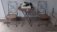Full set of two metal and wicker chairs with round wicker and metal table topped with faux flower bouquet