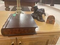 Photo showing all items on a wooden table: two bronze bulldog figurines, book-shaped box, and small carved decorative plate/box.