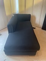 Front-side angle showing the black fabric chaise lounge with L-shaped backrest and cushioned seat.