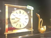 Photo showing Bulova mantle clock and one brass swan figurine on black surface