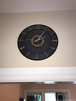 Front view of the wall mounted clock showing black face and gold numbers and hands.