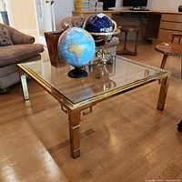 Overall view of square brass frame coffee table with glass top and decorative items on surface.