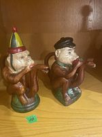Photo of two ceramic monkey figurines, one with a colorful pointed hat and the other with a black beret, both playing snake instruments.