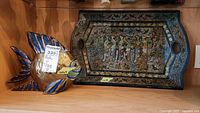 Display of the brass fish figurine next to the hand-painted bird-themed tray on a wooden surface.