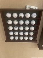 Front view of wooden golf ball display case holding 24 golf balls on five shelves.