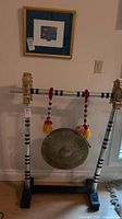 Full view of metal gong hanging on decorative wooden stand, two wands hanging from the stand