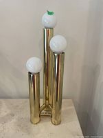 Front view of brass-toned MCM table lamp with three white globe bulbs on tubular stems.