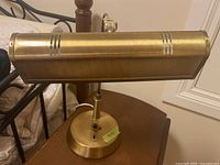 Brass banker's lamp top view showing rectangular shade with ventilation slots, mounted on curved arm and round base with control switches.