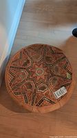 Top view of round leather ottoman showing starburst geometric pattern with fur insets and visible seam needing repair.