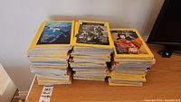 Several stacks of National Geographic magazines from the 1970s and 1980s arranged on a wooden table showing the sides and covers with the yellow borders.