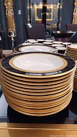 Stack of Noritake Opulence 9799 china bowls and plates showing black and gold decorative edges.