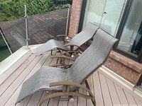 Pair of metal frame patio lounge chairs with grey woven mesh seating on a wooden deck near a glass railing.