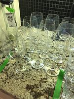 Top angled view of ten clear Riedel wine glasses on a granite countertop with a black backsplash in the background. Glasses have a round bowl and slender stem.