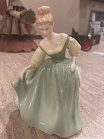 Front view of Royal Doulton figurine showing the lady holding her green dress skirt.