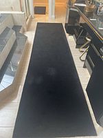Full view of the longer 15'x3' black runner rug laid out on a tiled floor with furniture and stairs visible in the background.