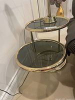 Side table showing upper and lower oval smoked glass surfaces with brass frame.