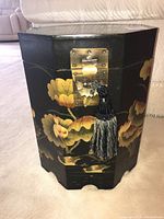 Front view of hexagonal black side table with floral painted design and metal latch with tassel.