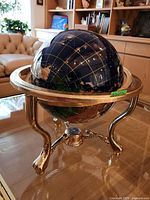 Full view of the globe mounted on a gold-colored metal stand with a compass detail on the base, placed on a glass table in a living room.