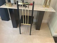 Photo of the metal chair with black frame, brass and silver backrest, black perforated seat, showing overall wear and condition.