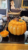 Photo showing the ceramic pumpkin tureen with lid and matching ladle on a glass table.