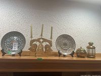Wide shot showing entire lot on wood surface including two plates on stands, brass candle holder, tealight lantern, brass container with lid, and matchbooks.