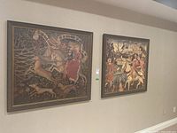 Two framed wall art pieces hung side by side on a beige wall, showing medieval-style figures, animals, and detailed nature backgrounds.