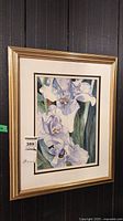 Full view of the framed watercolor painting depicting purple iris flowers hung on a dark vertically striped wall.
