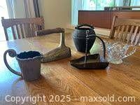Group photo showing pewter pitcher, antique Betty lamp, crystal sugar dish, stoneware vessel and brass shoe warmer on wooden table.