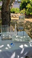 Wide shot of the full set on a white tablecloth outdoors, showing dispenser, decanter, tray with glasses, bottles in wire holder