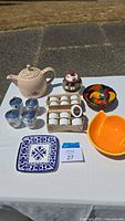 Wide shot of all items including teapot, bowls, sugar bowl, egg coddlers, and plates arranged on table outdoors.