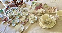 Wide view of 18 cups and saucers laid out on table, showing various patterns and colors.