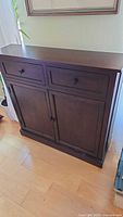 Front view of dark brown wooden buffet cabinet showing 2 drawers on top and 2 paneled doors below.