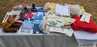 Wide view of embroidery and sewing supplies spread on a table including fabric, ribbons, buttons, hoops and threads.