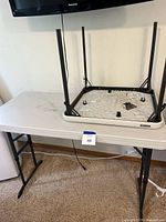 Two Lifetime folding utility tables with white plastic tops and black metal legs. One table shown upright and the other folded and resting on top.