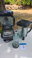 Ninja Professional blender base with glass container, second large blending container, and small blending cup on white surface outdoors.