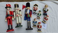 All nine wooden nutcrackers arranged on a white cloth, showing three large and six small sizes