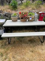 Outdoor picnic table and attached benches with garden decor on top, set on a grassy lawn.