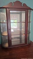 Front view of petite dark wood display cabinet with curved glass and decorative top