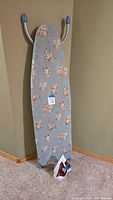 Rowenta steam iron at the base of a floral covered ironing board leaning against the wall, hooks at top visible