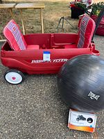 Red Radio Flyer two-seat plastic pull wagon with cushioned seats, shown outside on pavement with a wooden picnic table in background