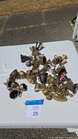 Full view of the assortment of vintage brass bells clustered on chains and placed on a white table outdoors.