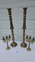 Two tall brass candlesticks and two brass candelabras grouped together, showing overall set size and condition.